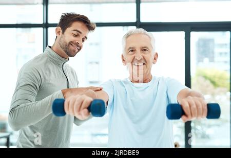 Pouvez-vous le sentir. Un kinésithérapeute sympathique aidant son patient senior à faire de l'exercice avec des poids. Banque D'Images