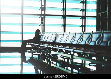 Il semble que la messagerie instantanée soit un peu tardive. Un voyageur non identifiable utilisant son smartphone dans un salon d'aéroport vide. Banque D'Images