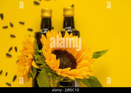 Huile de tournesol. Bouteilles d'huile, graines de tournesol noires éparpillées et tournesols fleurissant sur fond jaune vif.maquette d'huile de tournesol. Ferme naturelle Banque D'Images