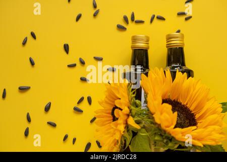 Des bouteilles d'huile, des graines de tournesol noires éparpillées et des tournesols fleurissent sur une huile de tournesol de ferme naturelle jaune vif de background.Organic. Huiles comestibles. Banque D'Images