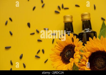 Huile de tournesol. Des bouteilles d'huile, des graines de tournesol noires éparpillées et des tournesols fleurissent sur une huile naturelle jaune vif de background.Organic. Huiles comestibles. Banque D'Images