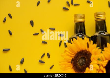 Huile de tournesol. Des bouteilles d'huile, des graines de tournesol noires éparpillées et des tournesols fleurissent sur une huile de tournesol de ferme naturelle jaune de background.Organic. Comestibles Banque D'Images