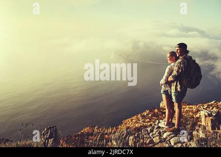 Découvrez l'amour dans les grands espaces. Un jeune couple aventureux admirant la vue depuis un sommet de montagne pendant une randonnée. Banque D'Images