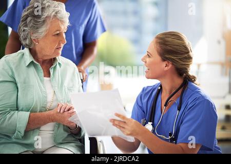 Garder ses patients en boucle. Un médecin discutant des traitements avec une femme âgée assise en fauteuil roulant dans un hôpital. Banque D'Images