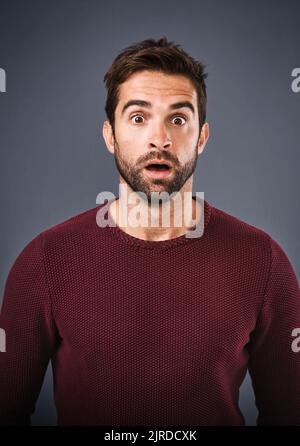 Ça. Soufflé. Photo studio d'un beau jeune homme à l'air surpris sur fond gris. Banque D'Images