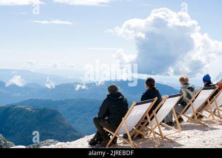 Groupe de personnes assis dans les chaises longues sur un sommet de montagne regardant les nuages au-dessus spectaculaire vue sur la montagne Banque D'Images