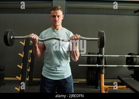 Portrait d'un jeune homme debout au club de santé et faisant des exercices avec la barbell Banque D'Images