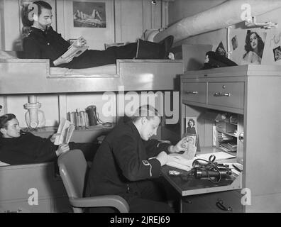 La Royal Navy pendant la Seconde Guerre mondiale Un agent's cabin à bord du HMS TRACKER lorsqu'elle s'est dans l'Atlantique Nord. Deux hommes sont couchés dans leur lit, tandis qu'un troisième siège écrit à son bureau. Banque D'Images