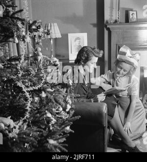 Fête de Noël pour le Cavalier Devereux's Daughter- Noël en temps de guerre, Pinner, Middlesex, décembre 1944 Mme Devereux et sa fille de 12 ans Jean s'asseoir tranquillement à côté de l'ensemble arbre de Noël pour lire un livre avant de se coucher après une petite fête de Noël à leur domicile de Pinner. L'arbre est un cadeau de son mari, actuellement en service dans l'armée à l'étranger, qui a été acheté par le biais du "Dons pour la Ligue d'accueil" de l'YMCA. Le livre qu'ils sont, c'est 'Mary Plain en temps de guerre", l'un des Jean's présente. Jean est encore vêtue de son chapeau de fête en papier. Banque D'Images