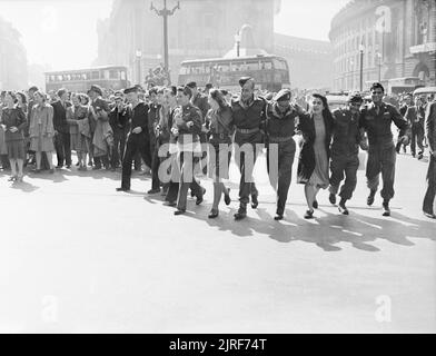 Les civils et le personnel de service in London's Picadilly Circus célébrer la nouvelle de la victoire des Alliés sur le Japon en août 1945. In London's Piccadilly Circus, un groupe de militaires hommes et femmes, et une femme, bras de liaison comme ils marchent vers l'appareil photo, chanter comme ils dansent dans la célébration autour d'Eros (pas sur la photo), sur la nouvelle que la guerre au Japon. Derrière eux, des foules de gens sont réunis sous le soleil. Plusieurs bus peut aussi être vu. Cette photo a été prise à côté de l'Éros, regard vers Piccadilly (à gauche) et Regent Street (à droite). Banque D'Images