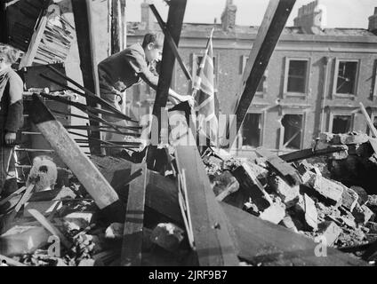 Londres montre les drapeaux- La vie continue en temps de guerre, Londres, Angleterre, 1940 Un jeune garçon appelé Leslie plante un drapeau de l'Union dans le tas de gravats et de débris, qui est tout ce qui reste de sa maison, à la suite d'un raid aérien sur Londres. Banque D'Images