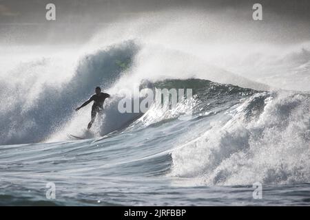 Un homme mince surfant sur les vagues mousseuse et haute barbotage dans la mer Banque D'Images