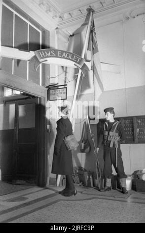 La jeune fille inconnue derrière la bataille de la mer- le travail de Women's Royal Naval Service, 1942 Wren Inconnu arrive à l'Eaglet HMS et doit montrer son col de la sentinelle de service. Le signe au-dessus de la porte dit 'Office de Tourisme d'un Officier général en charge'. Banque D'Images