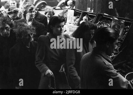 File d'attente des femmes pour les pommes de terre à un marchand de shopping à Londres au cours de 1945. Les femmes d'attente pour les pommes de terre dans un marchand de boutique, quelque part dans Londres. Un affichage de haricots peuvent seulement être vu à droite de la photographie. Les jardiniers peuvent seulement être vu servir un client dans le coin inférieur droit. Banque D'Images