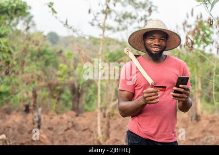 heureux agriculteur africain utilisant son téléphone et sa carte de crédit Banque D'Images