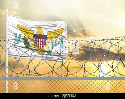 Mât avec le drapeau des îles Vierges des États-Unis contre le ciel et derrière une clôture avec fil barbelé. Le concept de protection du borde Banque D'Images