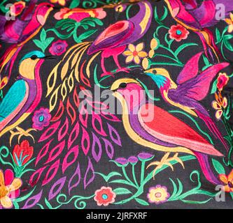 Tissu coloré fait main de Chiapas, Mexique. Oiseaux et fleurs aux couleurs variées sur fond noir. Banque D'Images