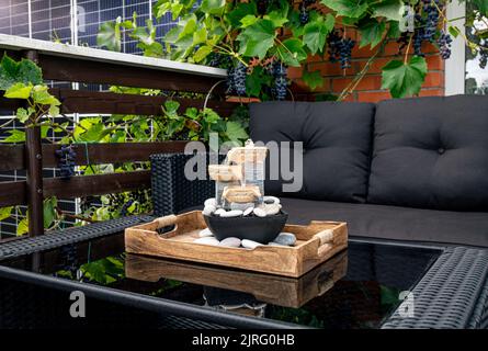 Maison patio avec meubles de jardin en plastique noir, petite fontaine de table zen électrique relaxante sur table et de vraies vignes avec des raisins suspendus. Banque D'Images