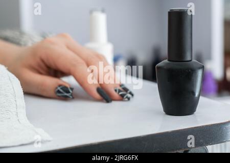 gros plan de vernis à ongles noir mat sur une table de manucure blanche, en arrière-plan une main avec des ongles peints en noir. concept de beauté et de style sombre. Banque D'Images