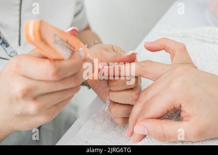 fille effectuant un limage d'ongles pour perfectionner et enlever les imperfections trouvées par le mauvais soin d'ongles. nettoyage avec lime d'ongles orange pour la manucure. Banque D'Images