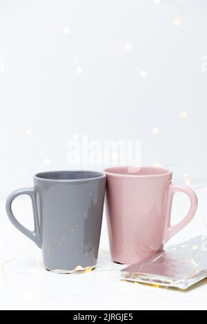 Deux tasses de café roses et grises mockup et une barre de chocolat sur fond blanc avec de petites lumières dorées et bokeh. Modèle vierge pour votre conception, votre marque, votre entreprise. Banque D'Images