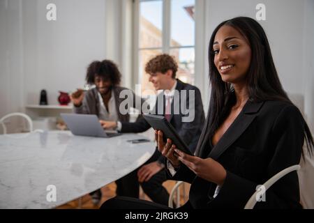 Portrait d'une femme d'affaires africaine au bureau vêtue avec élégance d'une tablette avec ses collègues en arrière-plan de travail Banque D'Images