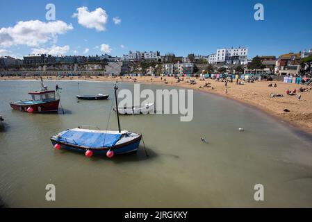 Bateaux à l'ancre tandis que les gens s'assoient sur la plage au soleil à Broadescaliers dans le Kent Angleterre Royaume-Uni Banque D'Images