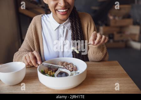Vue rognée pour une femme africaine souriant, souriant, tenant des couverts et goûtant des aliments diététiques sains au restaurant gastronomique Banque D'Images