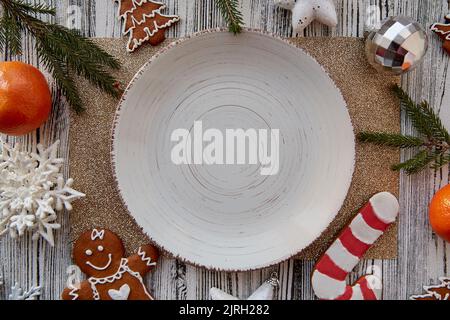 Table de Noël servie. Maquette d'assiette beige vintage, mandarines, pain d'épice fait main, biscuits, décorations de Noël sur la table. Jouets tendance pour arbres de Noël. Maquette esthétique. Vue de dessus. Banque D'Images