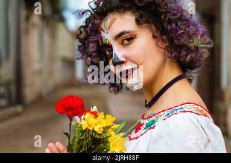 Portrait d'une jeune femme argentine du caucase du sud, tenant des fleurs avec ses mains debout à l'extérieur dans le cimetière avec le maquillage la Calavera Catrina, Banque D'Images