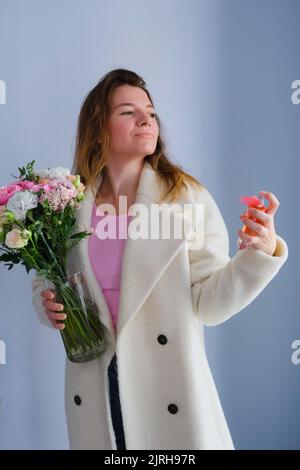 Portrait d'une femme heureuse posant dans des vêtements élégants avec des fleurs et une bouteille de parfum. Concept de mode créatif, mode de vie tendance Banque D'Images