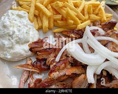 Gros plan de l'assiette de gyros de porc grec isolé prêt à manger avec des oignons, des frites et de la sauce tzatziki Banque D'Images