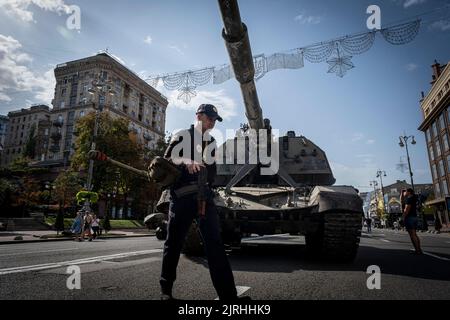 Un policier ukrainien muni d'un fusil passe devant une artillerie militaire russe détruite à Kiev. Consacrée à la prochaine Journée de l'indépendance de l'Ukraine, et près de 6 mois après l'invasion à grande échelle de l'Ukraine sur 24 février, la capitale du pays Kiev organise une exposition sur la rue principale de la rue Khreschaytk montrant plusieurs équipements militaires détruits, Chars et armes des forces armées de la Fédération de Russie (AFRF).alors que l'invasion russe complète de l'Ukraine a commencé sur le 24 février, la guerre qui a tué de nombreux civils et soldats, près de 9000 militaires ukrainiens Banque D'Images