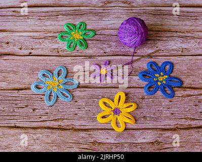 Fleurs crochetées et boule de fil violet sur fond de bois. Banque D'Images