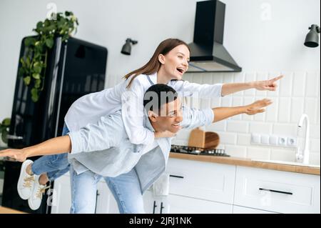 Joyeux couple dans l'amour, caucasien fille et un type hispanique, vêtu d'un vêtement moderne décontracté, s'amuser ensemble à la maison dans la cuisine, rire, profiter du week-end, éprouver des émotions positives Banque D'Images