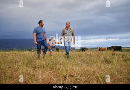 Famille d'agriculteurs marchant sur une ferme d'élevage ou d'élevage enseignant et apprenant ensemble. Des générations de liens heureux entre un père, un grand-père et un petit-enfant Banque D'Images