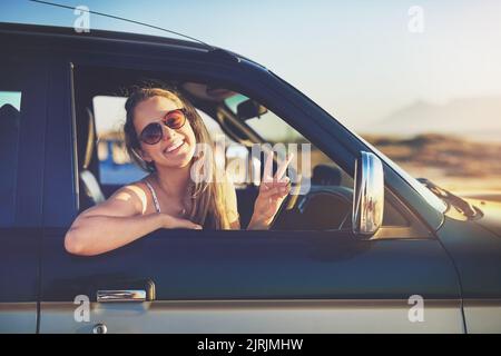 La paix à tous. Portrait court d'une jeune femme attrayante montrant un panneau en forme de pièce lors d'un voyage en voiture. Banque D'Images