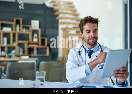 C'est un outil pratique pour stocker tous ses dossiers médicaux. Un jeune médecin travaillant sur une tablette numérique dans son bureau. Banque D'Images