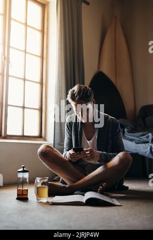 Ce week-end sera un pour les livres. Un jeune homme lisant un livre tout en étant assis sur le sol à la maison. Banque D'Images