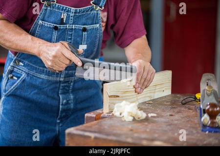 Un charpentier travaille avec de l'équipement sur une table en bois dans une boutique de menuiserie. Banque D'Images