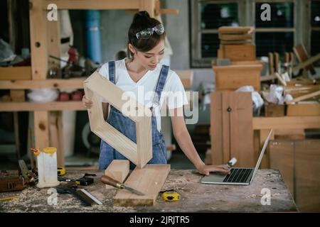Menuisier professionnel. Une femme travaille dans une boutique de menuiserie en utilisant une tablette pour concevoir des meubles dans une boutique de bois. Banque D'Images