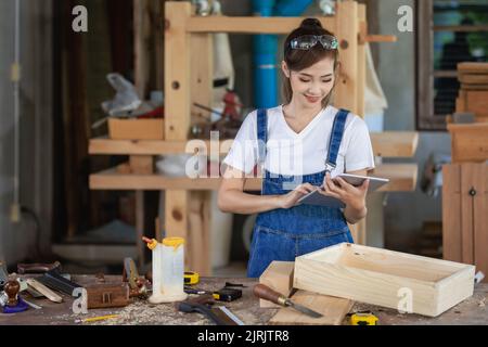 Menuisier professionnel. Une femme travaille dans une boutique de menuiserie en utilisant une tablette pour concevoir des meubles dans une boutique de bois. Banque D'Images