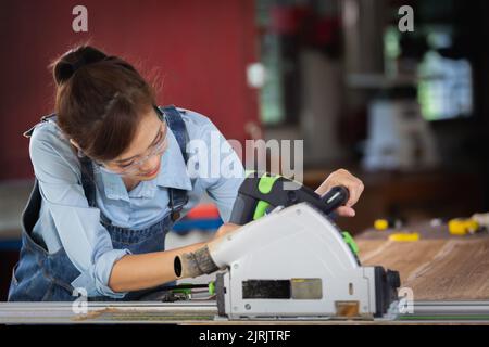 femme travaille dans une boutique de menuiserie. Charpentier féminin attrayant utilisant des outils électriques pour son travail dans un atelier de bois. Banque D'Images