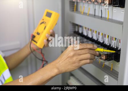 Testeur de travail électricien mesurant la tension et le courant de la ligne électrique d'alimentation dans le contrôle d'armoire électrique. Banque D'Images