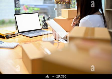 Active et réussie asiatique femme e-commerce entreprise de démarrage travaillant dans son bureau à domicile, la préparation de ses paquets d'expédition et de vérifier une commande en ligne Banque D'Images