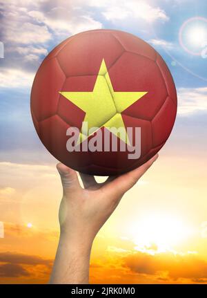 Ballon de football en main avec une représentation du drapeau du Vietnam contre un ciel coloré Banque D'Images