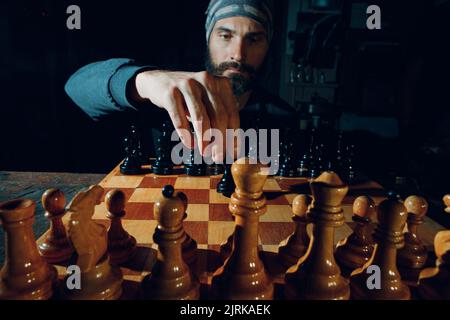 Jeune homme beau adulte jouant aux échecs dans l'obscurité. Figurines d'échecs et visage masculin à bord. Banque D'Images