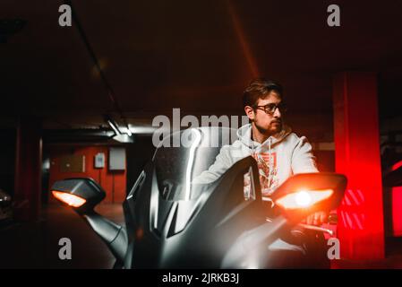 Jeune homme qui roule sur une moto à bord dans un parking sombre. Parking. Banque D'Images