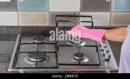 Une main de femme dans un gant en caoutchouc tient la grille du poêle à gaz pour laver la surface Banque D'Images