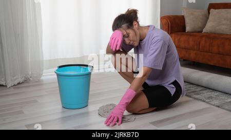 Une femme fatiguée en gants de caoutchouc lave le sol avec un chiffon sur ses genoux Banque D'Images